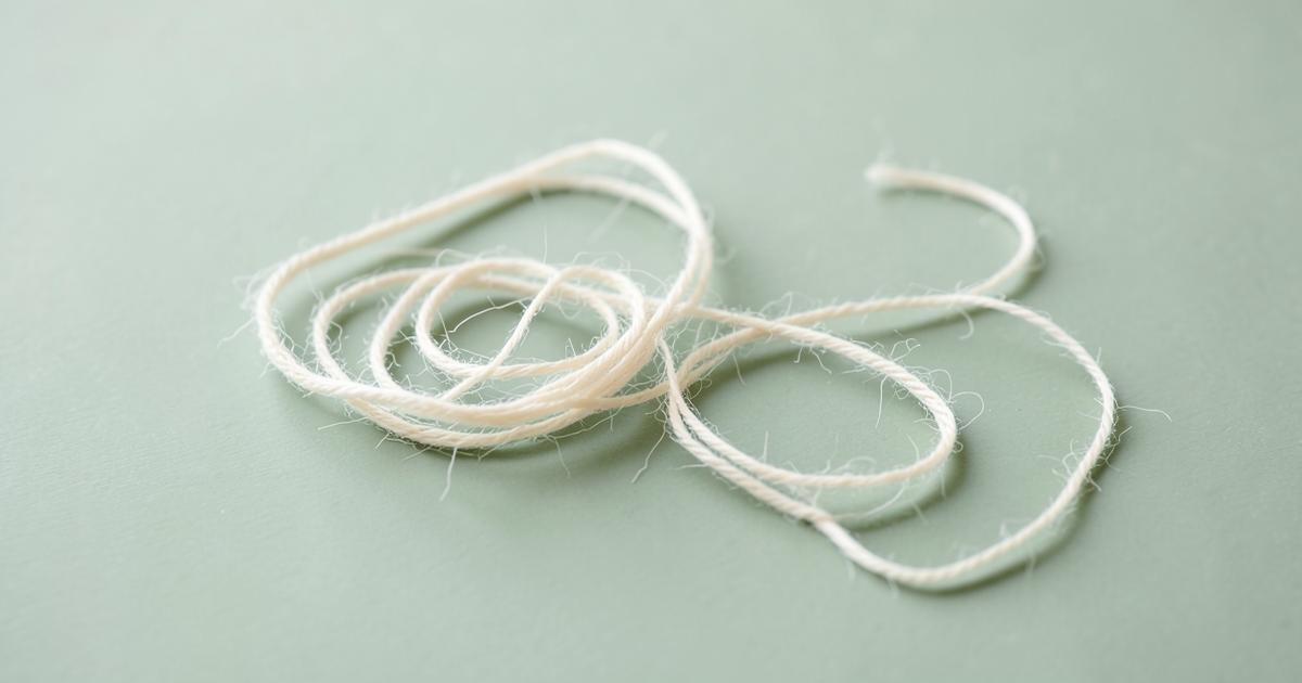 A loosely tangled cream thread beginning to unwind on a soft sage green surface